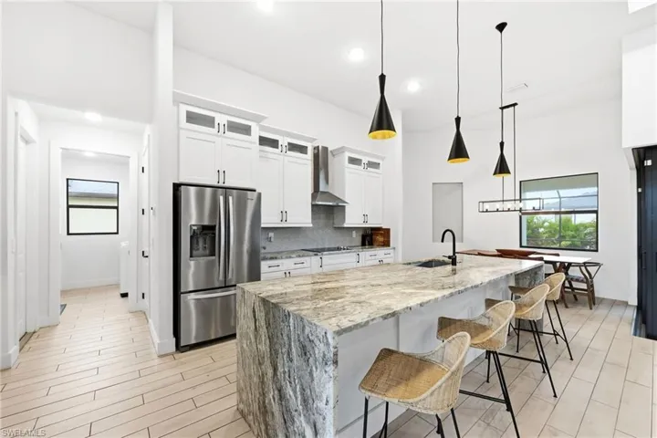 Kitchen featuring glass insert cabinets, a breakfast bar area, light stone countertops, white cabinets, and stainless steel fridge