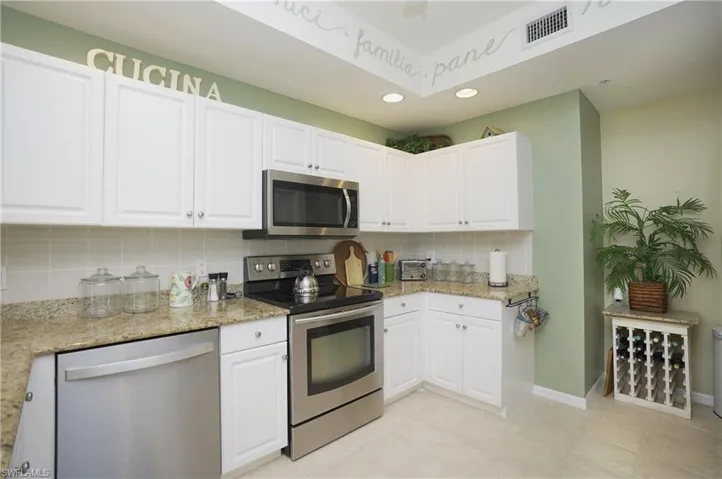 Kitchen featuring light stone counters, white cabinets, appliances with stainless steel finishes, and tasteful backsplash