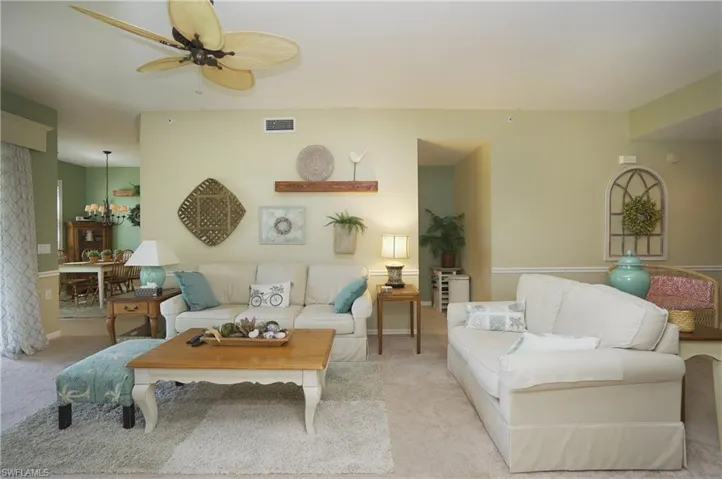Living room with ceiling fan with notable chandelier and light carpet