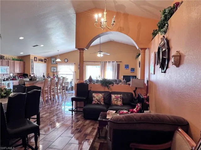 Living room featuring arched walkways, ceiling fan, decorative columns, a chandelier, and a textured wall