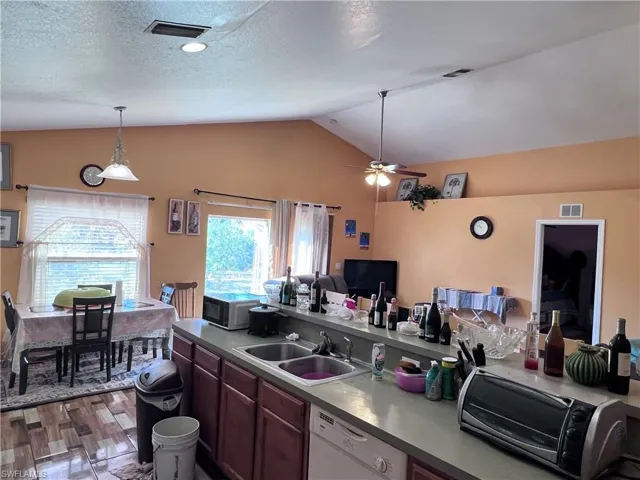 Kitchen with white dishwasher, ceiling fan, hanging light fixtures, dark wood-style flooring, and open floor plan