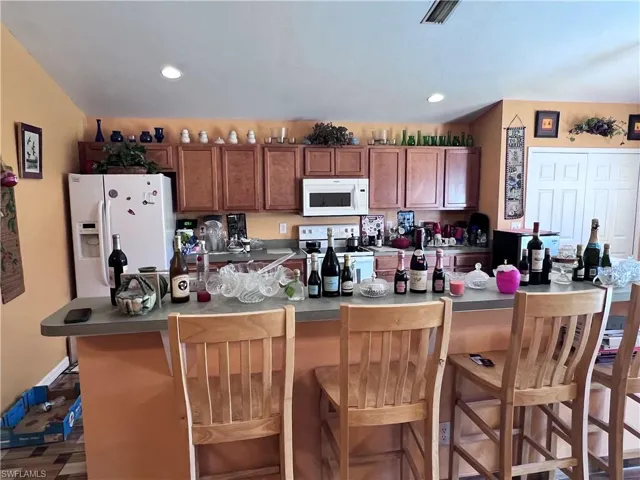 Kitchen featuring white appliances, wood finish cabinetry, a breakfast bar, dark countertops, and recessed lighting