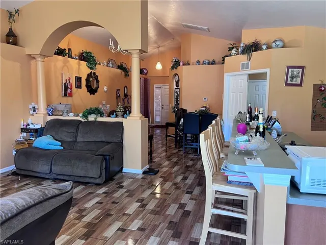 Living room with decorative columns, vaulted ceiling, wood finished floors, and arched walkways