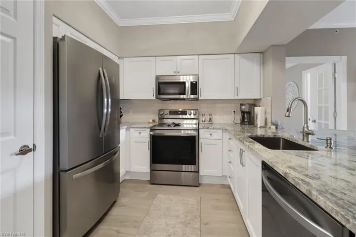 Kitchen with stainless steel appliances, white cabinets, sink, light stone countertops, and light hardwood / wood-style floors