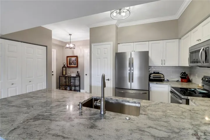 Kitchen with white cabinetry, tasteful backsplash, light stone counters, stainless steel appliances, and sink