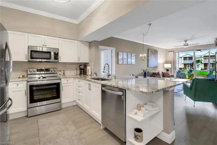 Kitchen featuring stainless steel appliances, sink, kitchen peninsula, light stone countertops, and ceiling fan with notable chandelier