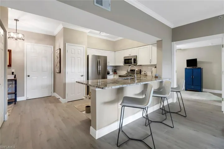 Kitchen with appliances with stainless steel finishes, stone countertops, white cabinets, and light wood-type flooring