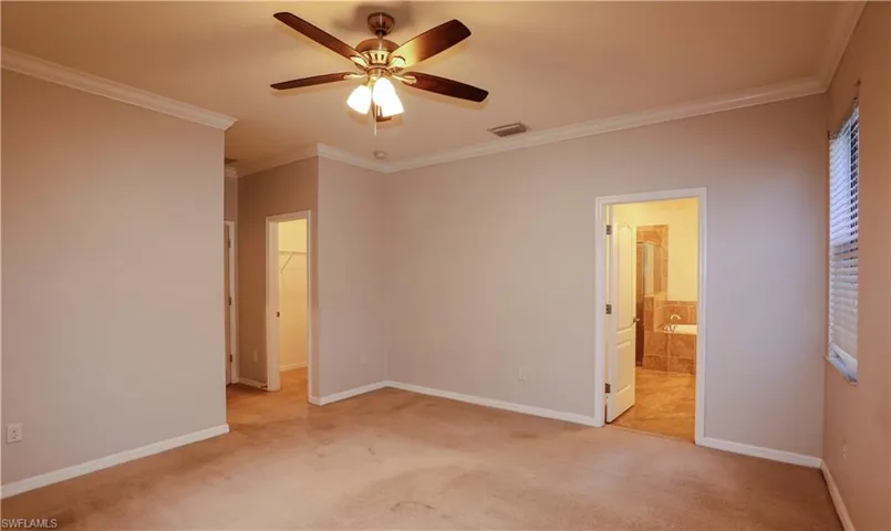 Neutral-toned interior featuring crown molding, a five-blade ceiling fan with integrated light fixture, carpeted flooring, and white interior doors