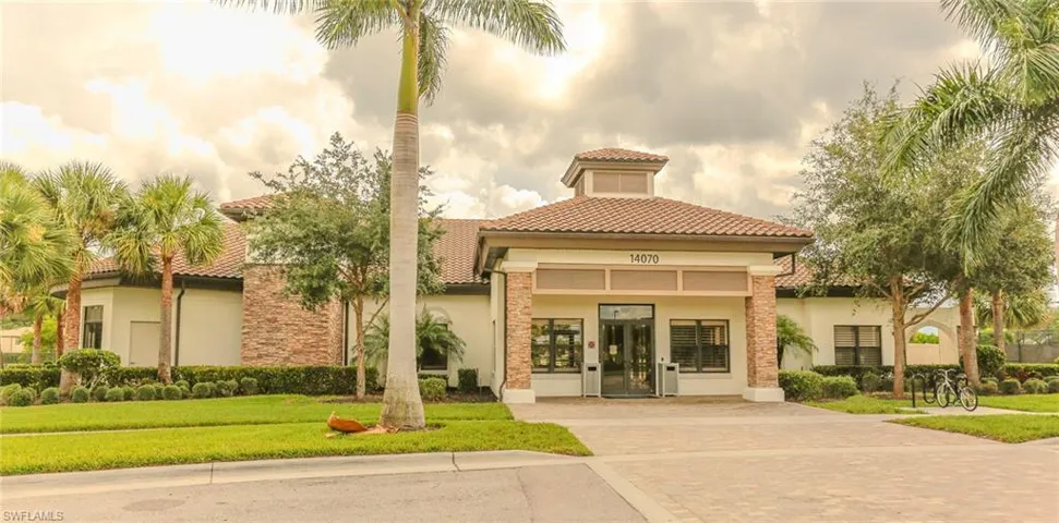 Stucco exterior building featuring a multi-tier tiled roof, stone masonry accents, a paved circular entryway, and manicured landscaping with palm trees