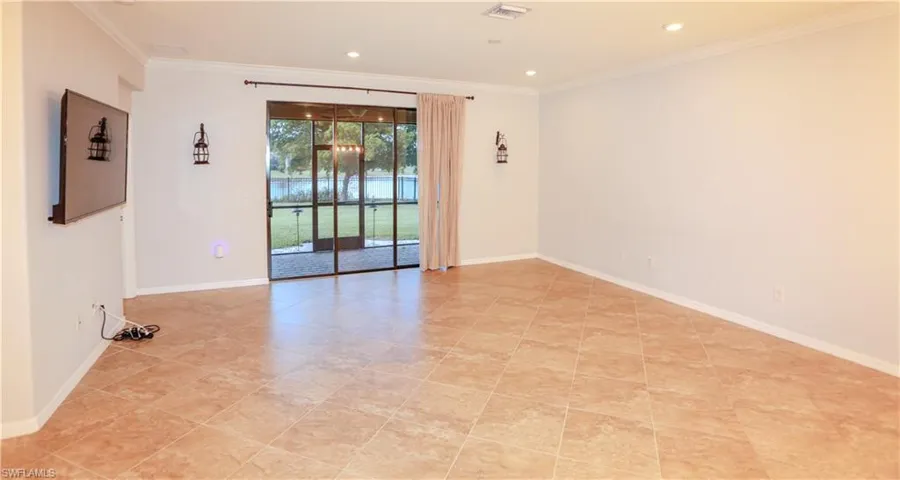Spacious room featuring diagonal tile flooring, recessed lighting, wall-mounted lantern-style sconces, and sliding glass doors with screen enclosure access