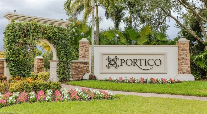 Community entrance featuring a stone-clad monument sign, arched stucco gateway, manicured landscape beds, and mature palm trees