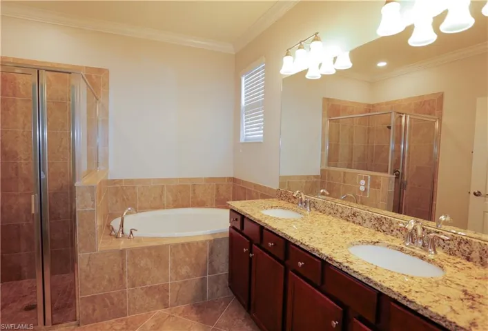 Double vanity with stone-patterned countertop and undermount sinks, custom dark wood cabinetry, soaking tub with tile surround, glass-enclosed walk-in shower, and large wall-mounted mirror