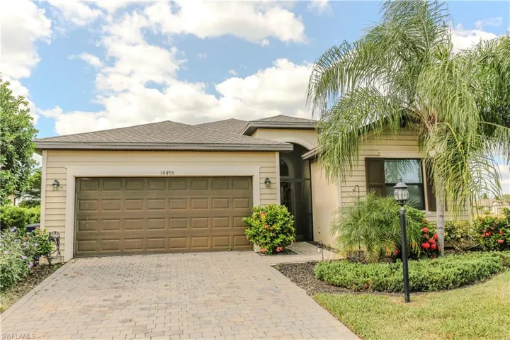 Single-story residence featuring a paver driveway, two-car garage, low-maintenance siding, arched entryway, and mature palm trees