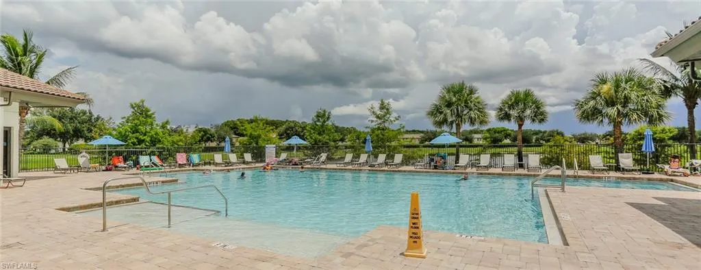 Outdoor swimming pool featuring a zero-entry ramp, metal handrails, paver decking, and perimeter fencing