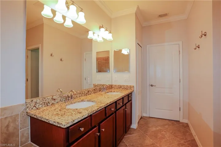 Double vanity featuring a stone-look countertop, dual undermount sinks, wood-finish cabinetry, tile flooring, and wall-mounted lighting