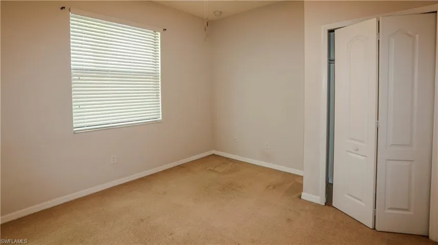 Interior space featuring neutral-toned carpeting, a single window with horizontal blinds, and a built-in closet with paneled bifold doors