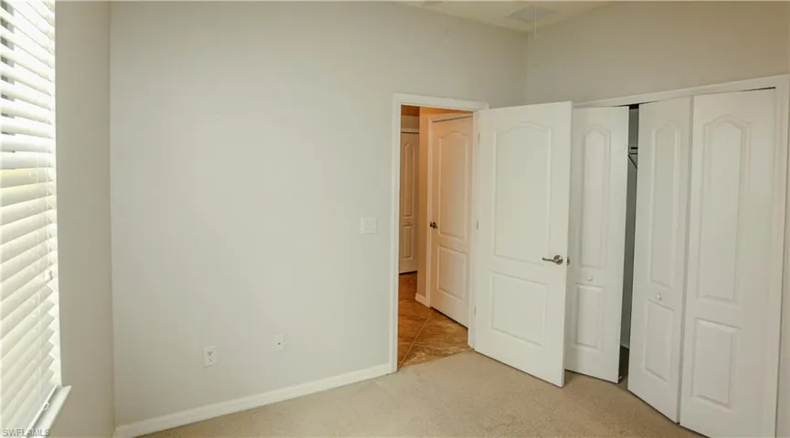 Neutral-toned interior space featuring beige carpeting, white two-panel doors, and white bi-fold closet doors with brushed nickel hardware