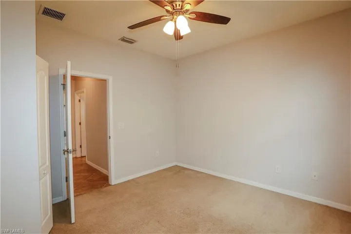 Neutral-toned interior space featuring carpeting, a multi-blade ceiling fan with integrated light fixture, and interior doors