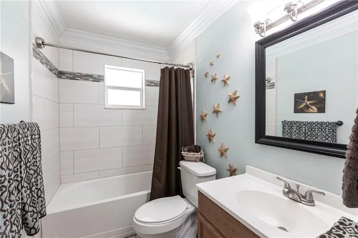Full bath featuring vanity, shower / bathtub combination with curtain, and ornamental molding