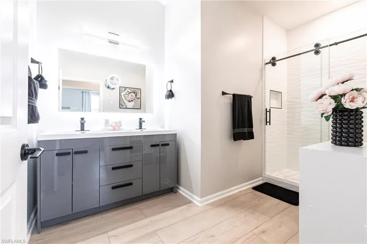 Full bath featuring double vanity, a stall shower, and light wood finished floors