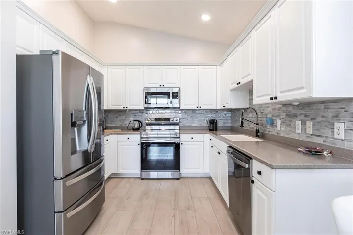 Kitchen with stainless steel appliances, white cabinetry, decorative backsplash, light wood-style floors, and lofted ceiling