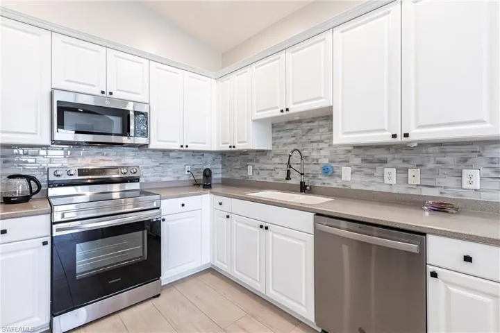Kitchen featuring stainless steel appliances, white cabinetry, backsplash, and light stone countertops