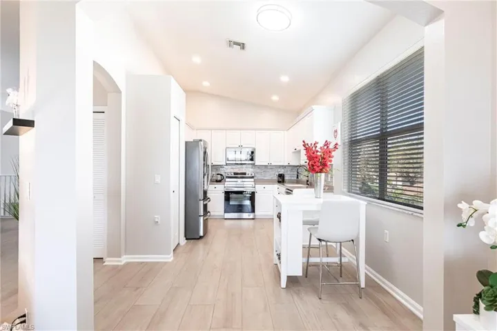 Kitchen featuring arched walkways, stainless steel appliances, white cabinets, light wood-type flooring, and a kitchen breakfast bar