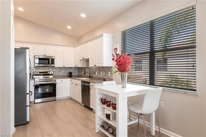 Kitchen with appliances with stainless steel finishes, backsplash, recessed lighting, vaulted ceiling, and white cabinets