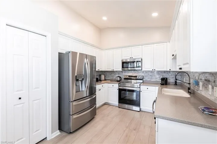 Kitchen featuring stainless steel appliances, tasteful backsplash, white cabinetry, light wood-style floors, and light stone countertops