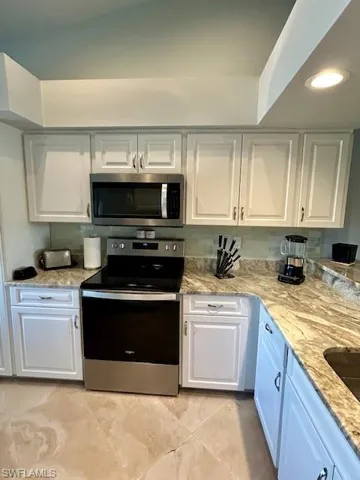 Kitchen with stainless steel appliances, white cabinets, light stone countertops, and recessed lighting