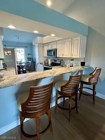 Kitchen featuring a breakfast bar, a peninsula, dark wood finished floors, and stainless steel appliances