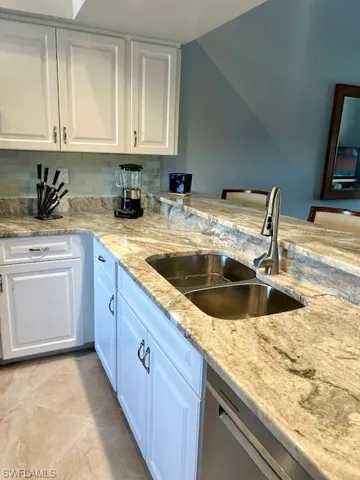 Kitchen with white cabinets, light stone counters, tasteful backsplash, stainless steel dishwasher, and a breakfast bar area