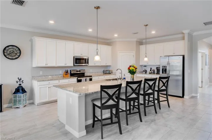 Kitchen featuring stainless steel appliances, a kitchen bar, white cabinetry, a large island, and ornamental molding