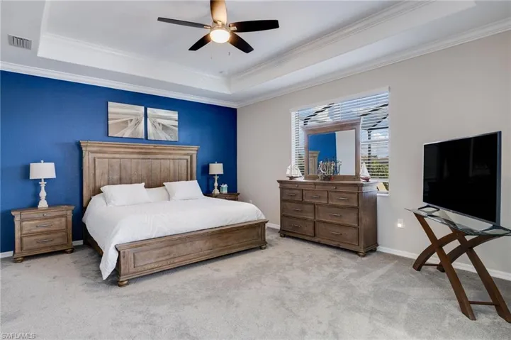 Bedroom with ornamental molding, ceiling fan, light colored carpet, and a raised ceiling