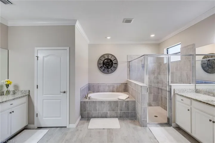 Bathroom with vanity, a stall shower, a garden tub, ornamental molding, and light wood-style flooring