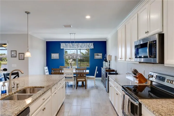 Kitchen featuring stainless steel appliances, white cabinetry, light stone counters, and ornamental molding