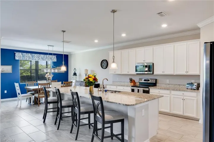 Kitchen with a breakfast bar, stainless steel appliances, white cabinets, crown molding, and a center island with sink