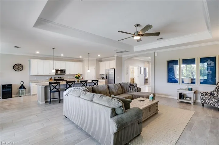 Living room featuring crown molding, arched walkways, ceiling fan, a raised ceiling, and wood finish floors