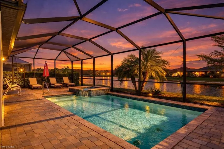 Pool at dusk with a lanai, a pool with connected hot tub, a sunroom, and a water view