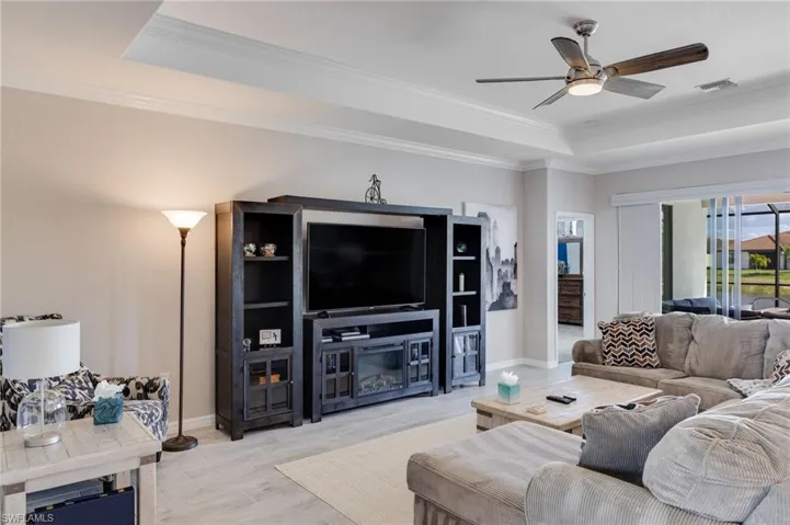 Living area featuring crown molding, a ceiling fan, light wood-type flooring, and a raised ceiling