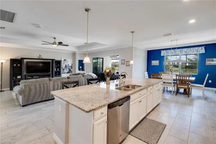 Kitchen with white cabinetry, stainless steel dishwasher, light stone countertops, crown molding, and open floor plan