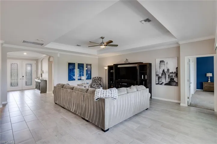 Living room featuring arched walkways, french doors, a tray ceiling, ornamental molding, and a ceiling fan