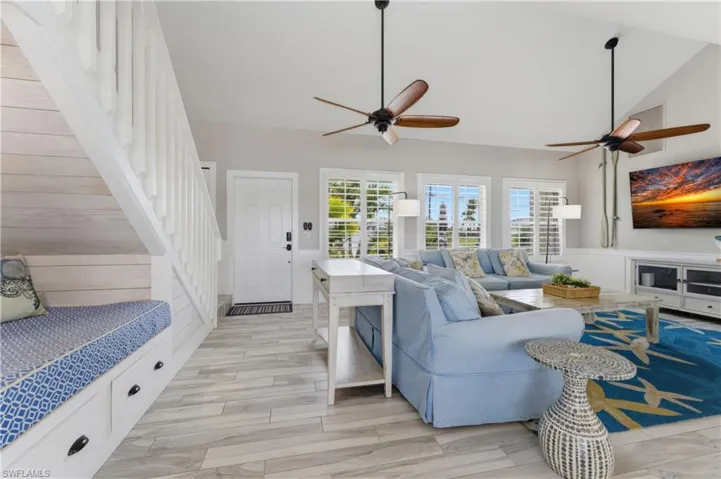 Vaulted ceiling living area featuring multiple windows with plantation shutters, wood-finish flooring, and two ceiling fans