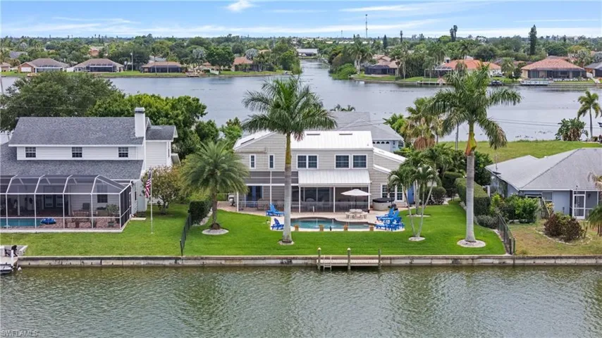 Waterfront property featuring a private boat dock, lush green lawn, and mature palm trees