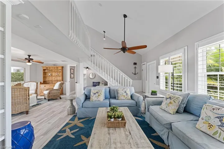 Vaulted ceiling living area featuring light wood-finish flooring, white plantation shutters, and a white staircase with open railings