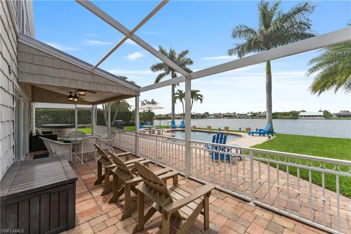 Outdoor patio with brick pavers, screened lanai, and waterfront access featuring a swimming pool and mature palm trees