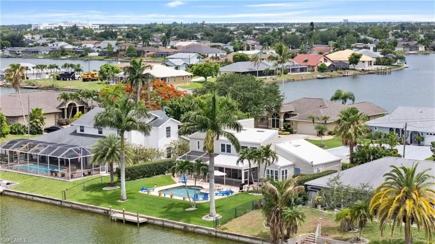 Waterfront property featuring a screened-in pool, private dock, manicured lawn, and mature palm trees