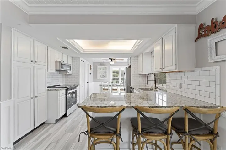 Kitchen featuring white shaker cabinetry, subway tile backsplash, granite countertops, and wood-finish flooring
