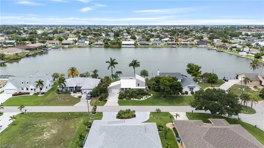 Waterfront property featuring a private boat dock, mature palm trees, manicured landscaping, a paved driveway, and a concrete patio