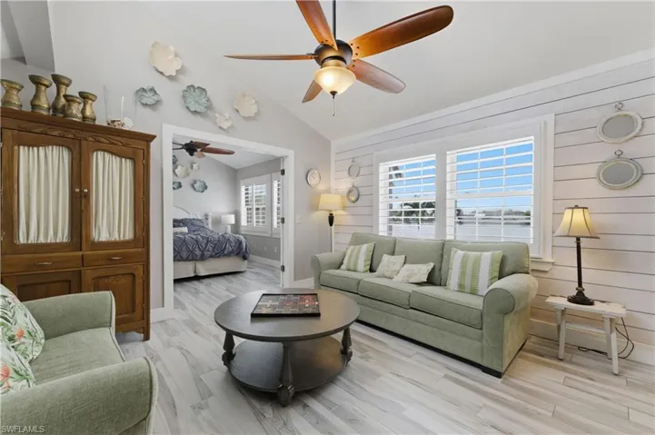 Living area featuring vaulted ceilings, wood-finish flooring, a ceiling fan, and white shiplap accent walls